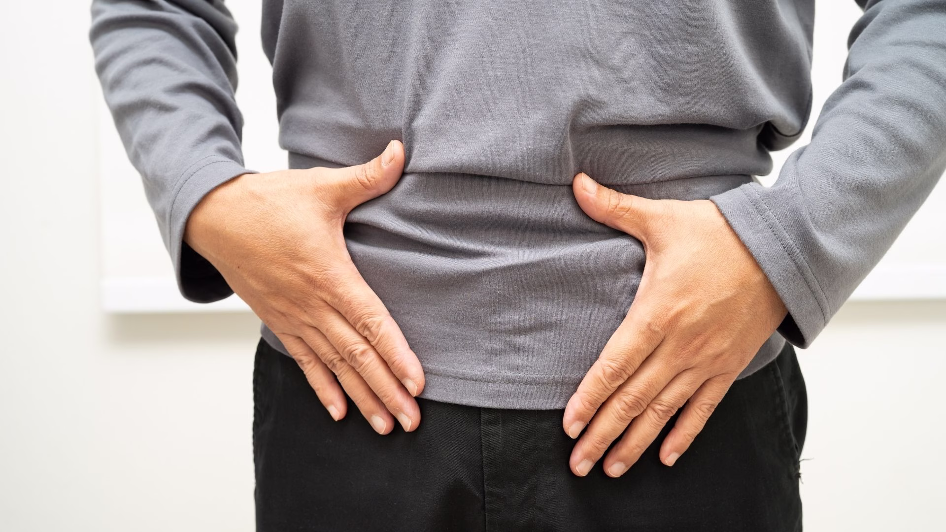 Adult holding the lower abdomen near the groin, where a femoral hernia can cause discomfort